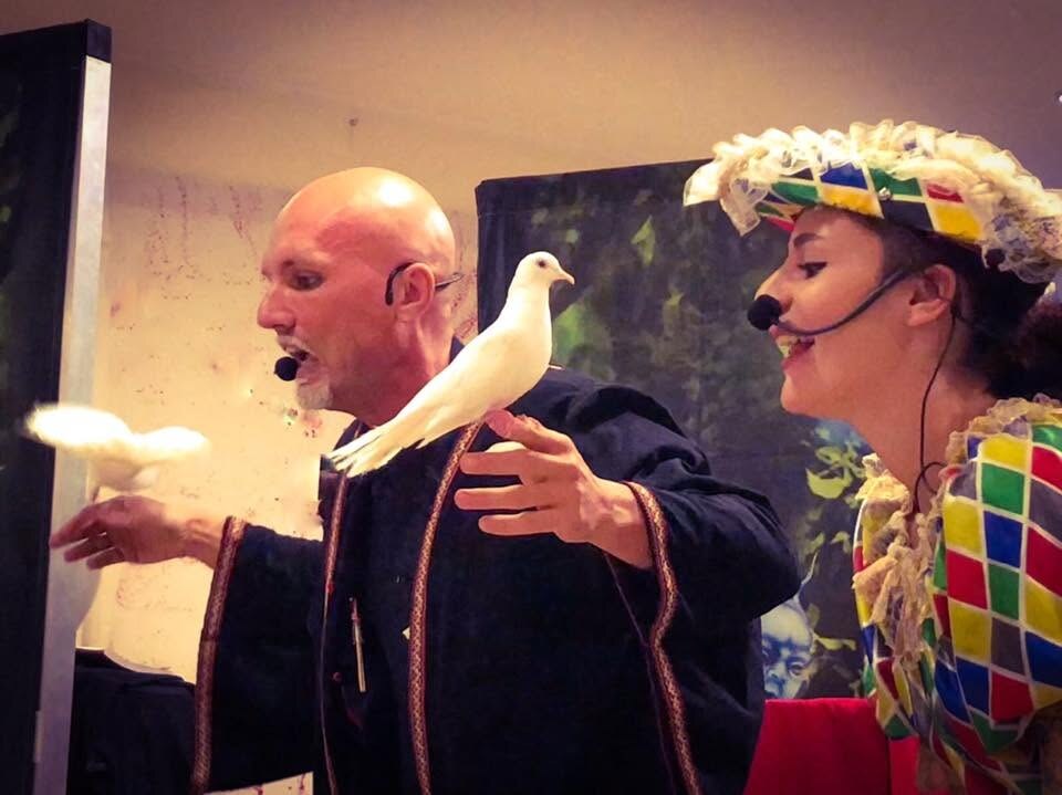 Guglielmo Wilson e Arlecchina sul palco con colombe bianche durante lo spettacolo