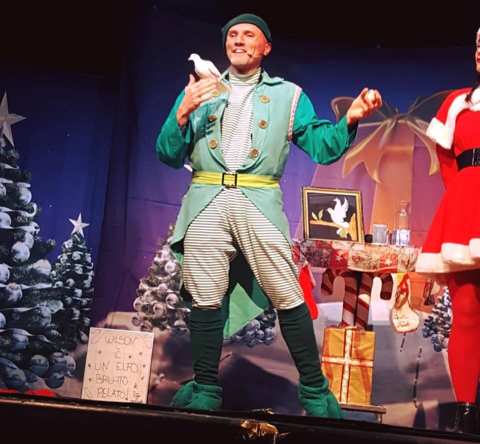 Guglielmo Wilson in costume da elfo con una colomba bianca durante uno spettacolo di Natale